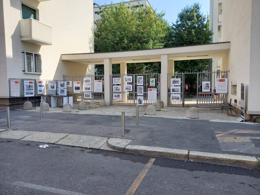 Veduta d'insieme dell'allestimento all'ingresso di via Birago 2: i pannelli e le fotografie in bianco e nero disposti lungo la cancellata e sotto il portico