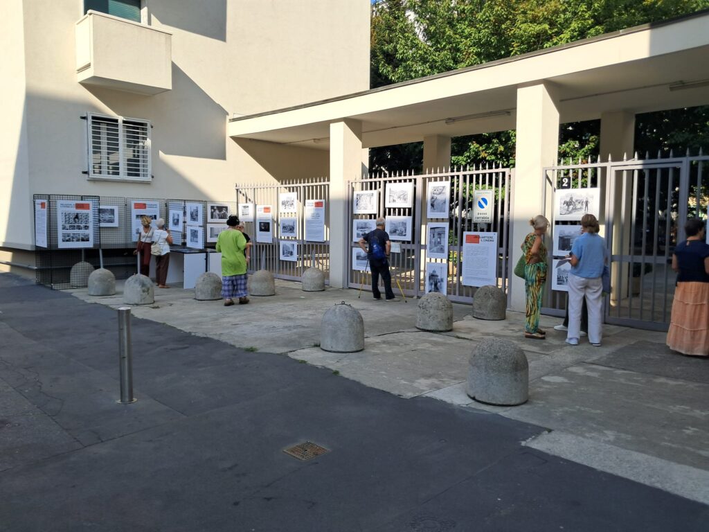 Alcune persone osservano i pannelli e le fotografie appesi alla cancellata di via Birago 2, nel pomeriggio.