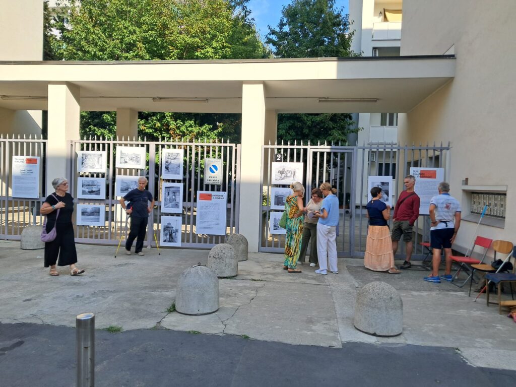 Un gruppo di visitatori davanti all'ingresso della mostra; alcuni conversano tra i dissuasori in pietra.